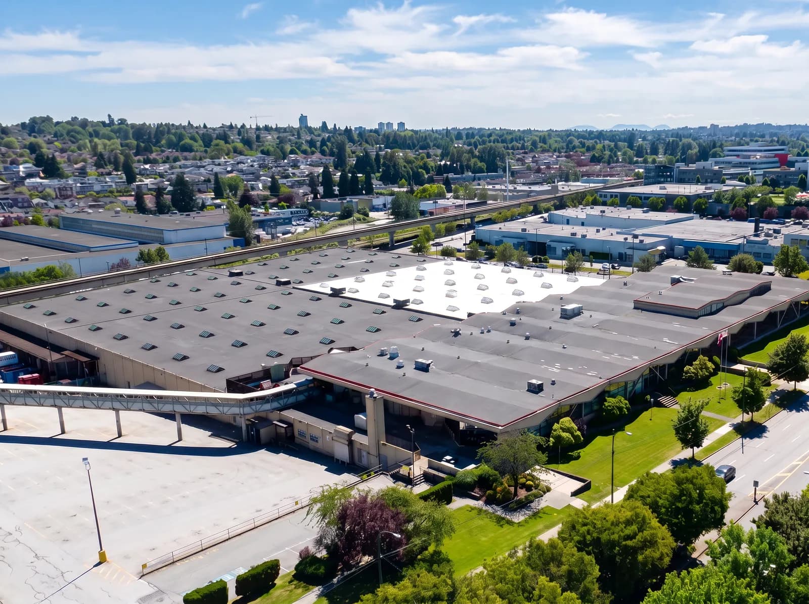 Aerial view of the Rolls Right warehouse building at 3200 E Broadway in Vancouver, with the SkyTrain corridor and city beyond