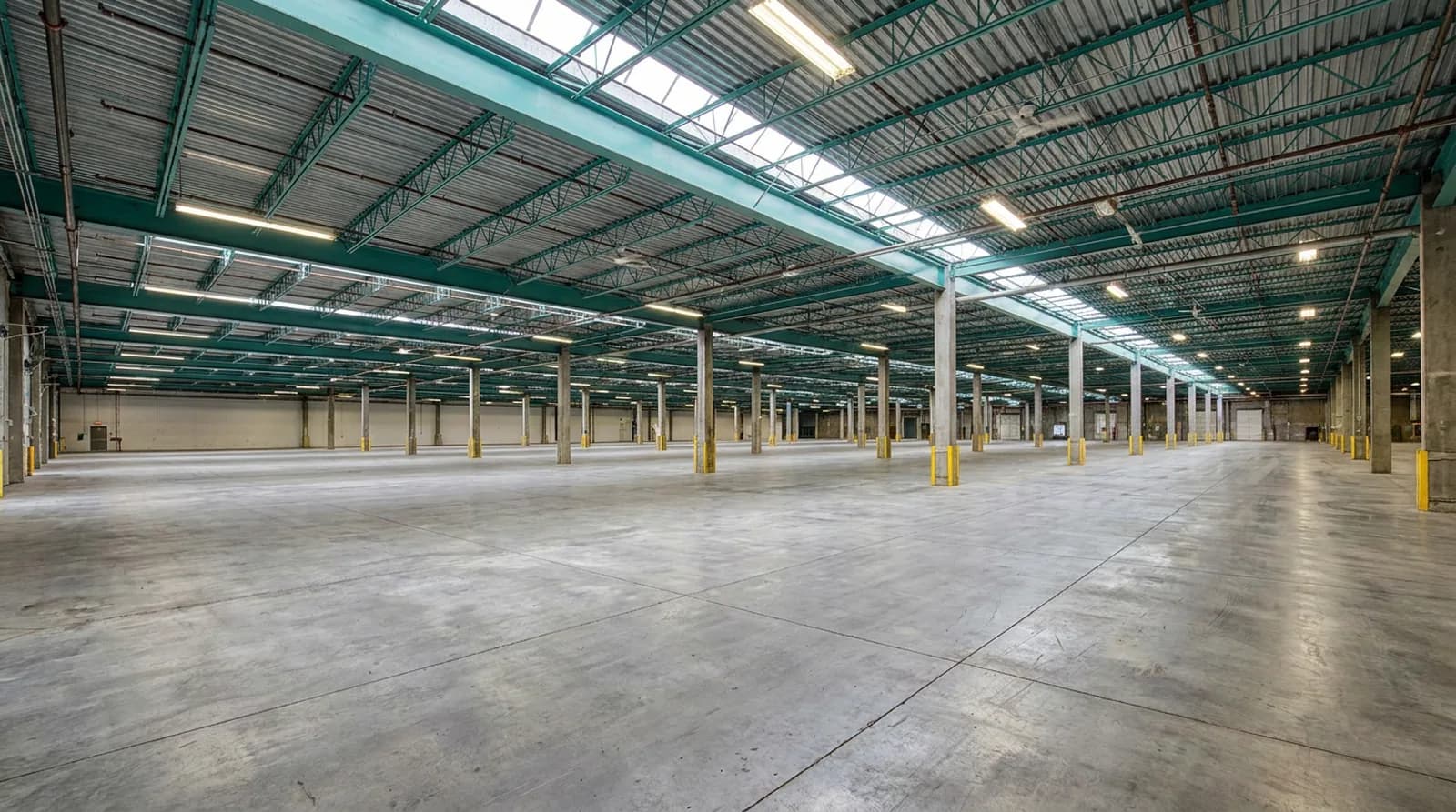 The empty floor of the Rolls Right Vancouver warehouse between painted steel roof joists and concrete columns