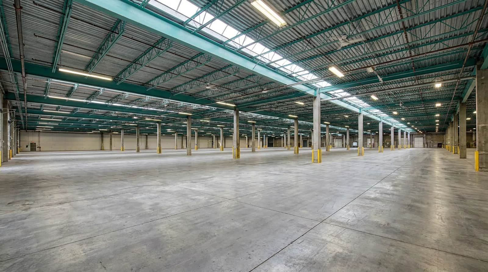 The empty floor of the Rolls Right Vancouver warehouse, looking diagonally across the concrete slab between painted steel roof joists and concrete columns
